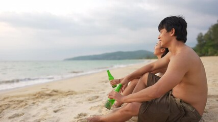 Wall Mural - Group of Happy Asian man and woman friends sitting on the beach enjoy drinking beer with talking together at summer sunset. Male and female friendship relax and having fun outdoor lifestyle activity.