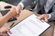 © ABCreative - Older man, mature boss in suit sits at desk in office, hands contract on pad to sign to new employee with other hand shake congratulations, close-up of document