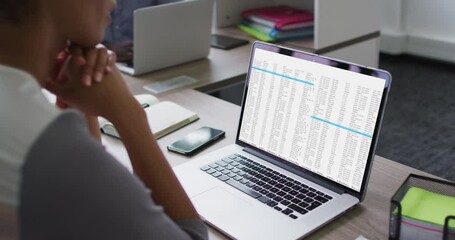 Mixed race woman sitting at desk watching coding data processing on laptop screen
