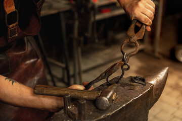 Close-up hands of male blacksmith forge an iron product in a blacksmith. Hammer, red hot metal and anvil. Concept of labor, retro professions