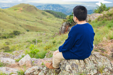 boy sitting on the rock looking at the landscape