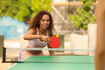 Poster - African-American woman playing ping pong with friend outdoors