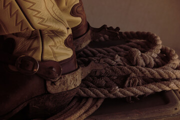 Canvas Print - Dark moody western ranch still life with cowboy boots and spurs by old rope.