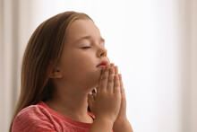 Cute Little Girl With Hands Clasped Together Praying On Blurred Background. Space For Text
