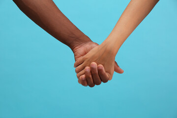 Wall Mural - Woman and African American man holding hands on light blue background, closeup