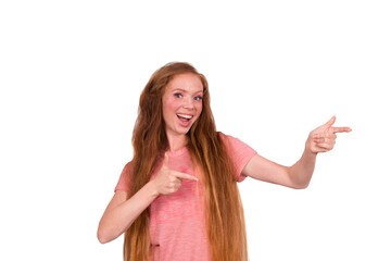 Cheerful redhead girl with long hair, points to the side to the place for text, discusses amazing promo, gives way or direction, smiles confidently and happily, isolated on white background