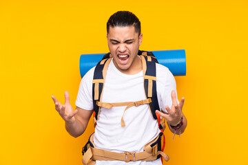 Wall Mural - Young mountaineer asian man with a big backpack isolated on yellow background unhappy and frustrated with something