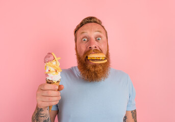 Hungry man with beard and tattoos is undecided if to eat an icecream or a sandwich with hamburger