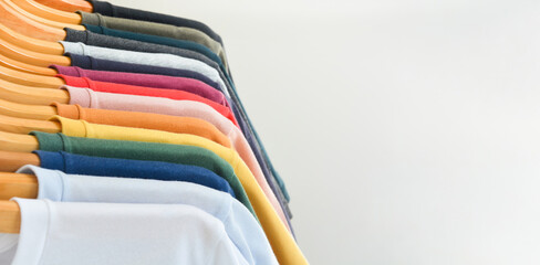 close up collection of color t-shirts hanging on wooden clothes hanger in closet or clothing rack ov