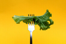 A Leaf Of Green Lettuce Is Planted On A Fork On A Yellow Background.