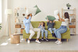© Studio Romantic - Happy family of four having fun on sofa at home. Excited cheerful mommy, daddy and two children having a pillow fight and laughing sitting on couch in modern cozy Scandinavian living room interior