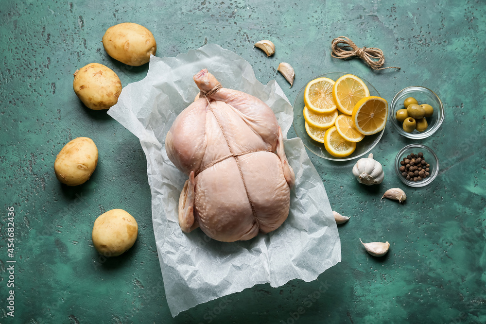 Parchment with whole raw chicken, lemon, vegetables and spices on color background