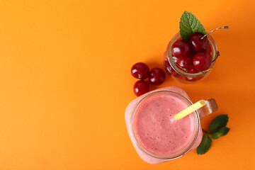 Wall Mural - Glass jar of cherry smoothie and ingredients on orange background