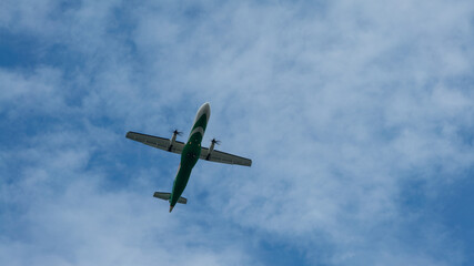 Wall Mural - View of propeller plane flying low with blue sky and clouds at background.
