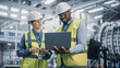 © Gorodenkoff - Two Diverse Professional Heavy Industry Engineers Wearing Safety Uniform and Hard Hats Working on Laptop Computer. African American Technician and Female Worker Talking on a Meeting in a Factory.