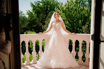 Wall Mural - the bride in a white lace dress and a long veil stands on the terrace.