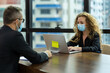 © amorn - Business man and business woman wearing protective medical face mask, wearing formal suite, sitting and working with computer laptop in the modern office. health, businesspeople and office concept