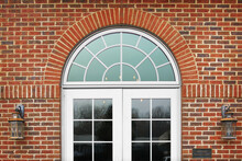 Double White Glass French Doors With Half Circle Window Grill Design On Brick Building With Lanterns