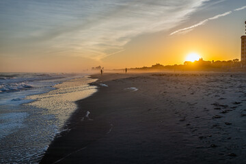 Wall Mural - Colorful sunset at Myrtle Beach city by Atlantic ocean with sun behind horizon by condo condominium apartment buildings, people silhouettes walking by crashing waves in resort South Carolina town