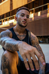 Wall Mural - Vertical shot of a Caucasian sporty male with tattoos and glasses looking at the camera