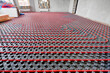Installation of a heat flooring system in a country house under construction. Red tubes for floor heating. Modern heating system of a country house