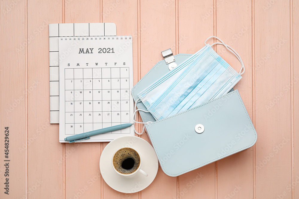 Calendar with cup of coffee, bag and medical masks on color wooden background