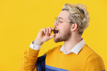 Handsome Young Man Eating Chocolate Candy On Color Background