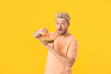 Wall Mural - Handsome young man eating tasty nachos on color background