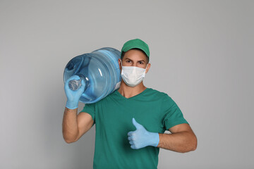 Sticker - Courier in medical mask with bottle for water cooler showing thumb up on light grey background. Delivery during coronavirus quarantine