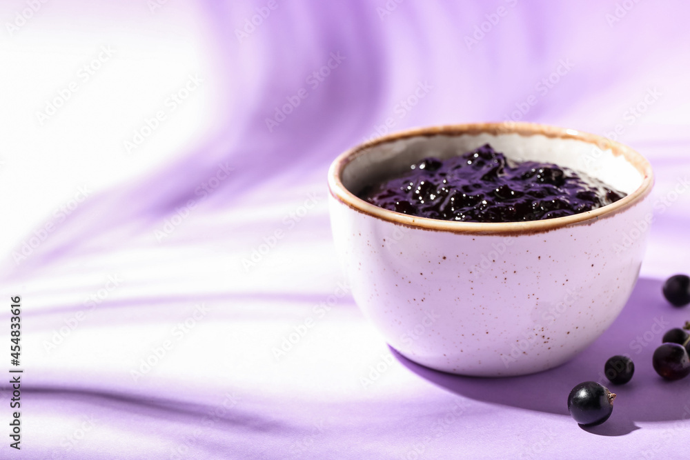 Bowl with black currant jam on color background