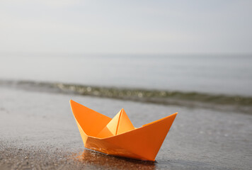 Orange paper boat on sandy beach near sea, space for text