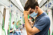 © URI - Young dark-haired boy in navy blue t-shirt with mask making a headache gesture in the subway