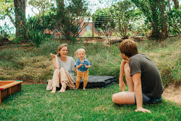 Wall Mural - Happy family with little child resting on backyard. Woman sitting with daughter on mattress and looking at man sitting back to camera. Family outdoor concept