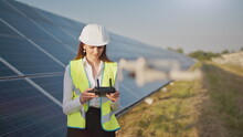 Portrait Of A Female Engineer Operating A Drone On The Background Of A Solar Power Plant. Solar Panel Array Installation. Technologies And Ecology. Sunsets.
