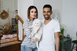 Lovely mixed-races young happy joyful couple male and female smiling in good mood resting at home in living room with pet animal holding cat in hands, pet lover concept