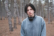 Teenage boy 16-17 year old wear sweatshirt and headphones posing in woods looking at camera. Sad serious guy outdoors.