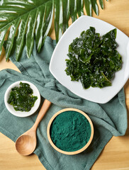 Top view laminaria or kelp seaweed and spirulina powder in wood bowl and spoon background. flat lay spirulina powder with konbu and alga food on wood table background.