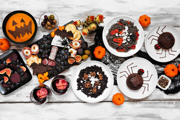 Wall Mural - Halloween dinner party table scene over a white wood background. Top view. Spooky black risotto and pasta, charcuterie board, jack o lantern pumpkin soup, spider cakes, and apple skull wine.