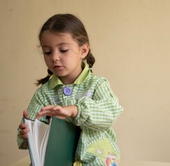 Canvas Print - Cute little girl with pigtails sitting in a classroom and opening a book