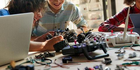 School kids boys helping building robotic car learning together at STEM class. Happy students children study together making robots in classroom at science and coding education lesson, close up view.