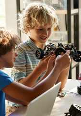 School kids boys helping in building robotic car learning together at STEM class. Happy students children studying together playing making robots in classroom at science and coding education lesson.