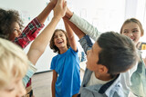 Fototapeta  - Happy diverse multiethnic kids junior school students group giving high five together in classroom. Excited children celebrating achievements, teamwork, diversity and friendship with highfive concept.