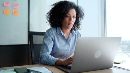 Wall Mural - Young African American focused female executive manager businesswoman sitting at desk working typing on laptop computer in contemporary corporation office. Business technologies concept.