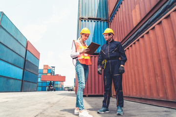 Industrial worker works with co-worker at overseas shipping container yard . Logistics supply chain management and international goods export concept .