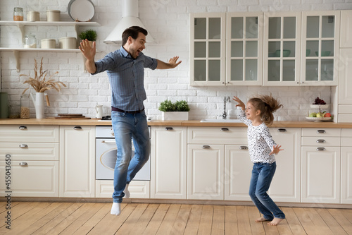 Excited crazy dad teaching daughter girl to dance at home. Active funny daddy and energetic kid exercising together in kitchen, listening to music, having fun, jumping in wild dance, laughing