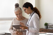 © fizkes - Serious GP doctor showing tablet screen to old 70s female patient, explaining electronic prescription, medical screening, examination result, giving consultation. Woman visiting practitioner