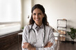© fizkes - Happy female GP doctor in white coat with stethoscope looking at camera, smiling. Head shot portrait of confident medical practitioner, physician, therapist posing in hospital office with arms folded