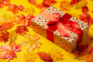 Wall Mural - Romantic gift box with autumn leaves on yellow background. Top view