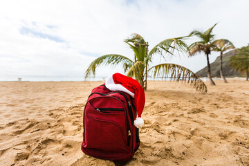 Santa Claus hat on backpack standing on sand beach. Christmas and New Year celebration. Nobody.