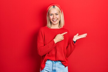 Poster - Beautiful blonde woman wearing casual red sweater amazed and smiling to the camera while presenting with hand and pointing with finger.